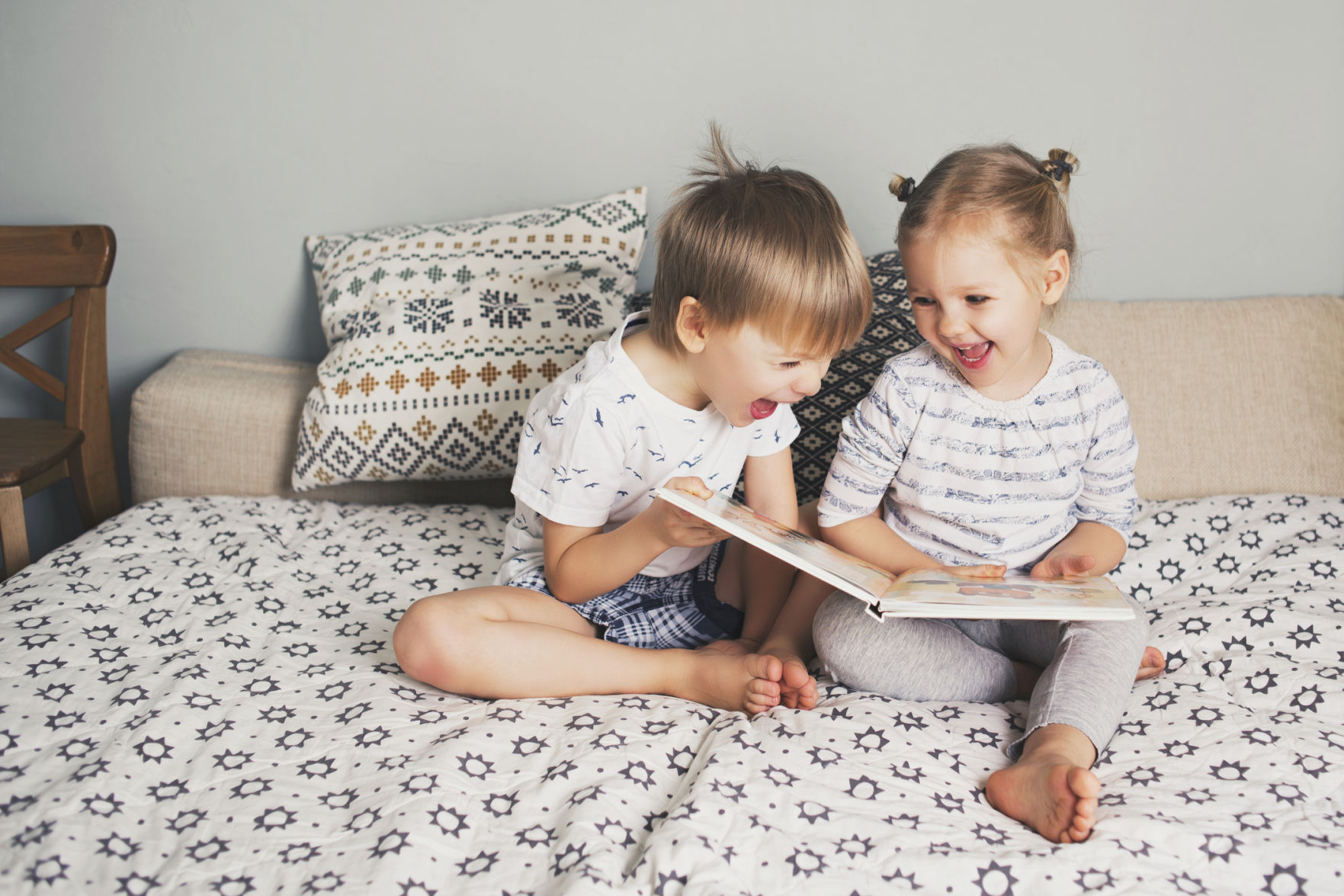 Two kids sitting on bed and reading a book